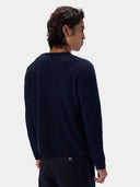 A man shown from the back wearing a navy blue long-sleeve crewneck knit sweater and dark trousers, against a light gray studio background.