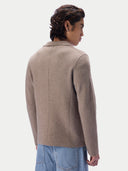 A man shown from the back wearing a taupe knit blazer-style cardigan and light blue jeans, against a light gray studio background.