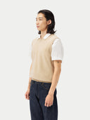 close up side view of man wearing a beige v-neck vest over a white polo shirt and jeans  #color_beige