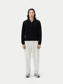 front view of a person wearing a black cashmere polo sweater with a collar and white pants, standing against a plain background.  #color_black