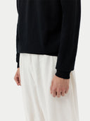close up of a black long sleeve sweater detail and white pants on a gray background #color_black