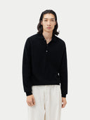 close up of A person wearing a black cashmere polo sweater with a collar, standing against a plain background.  #color_black