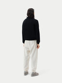 back view of a person wearing a black cashmere polo sweater with a collar and white pants, standing against a plain background.  #color_black