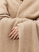 Close-up of a person wearing a beige coat with a hand peeking out from the blanket. #color_beige