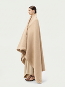Side view of a woman wearing a beige cape on a white background. #color_beige