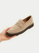 Beige loafer shoe held in a hand against a light background #color_warm-grey