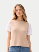 close up front view of a woman wearing a beige sleeveless sweater over a white t-shirt and blue jeans on a white background #color_beige