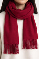 close up of a red scarf with fringes worn by a person on a white background bordeaux