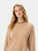 A zoomed-in shot of a model in a beige knit dress and a thick gold chain necklace. #color_beige