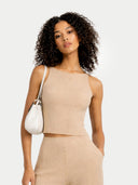 Woman wearing a beige sleeveless top and pants with a white handbag on a light gray background #color_beige
