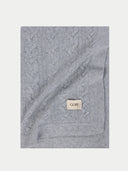 Gray cable knit blanket with a brand label on a white background #color_high-rise