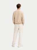 back view of a Person wearing a beige sweater and white pants on a light gray background #color_beige