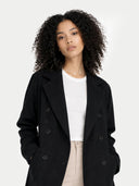 Woman wearing a black coat over a white shirt with a plain background  #color_black