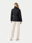 Back view of a person wearing a black quilted jacket and white pants on a light gray background #color_black