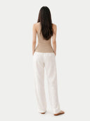 back view of Woman wearing a beige top and white pants on a plain background #color_warm-grey
