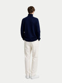 back view of a person wearing a navy sweater and white pants on a white background