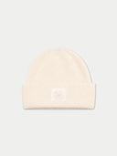 A cream-colored ribbed knit beanie hat with a small tonal embroidered clover logo on the front cuff, set against a solid light gray background.