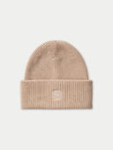 A ribbed knit beanie in a warm beige or light tan color, featuring a small white embroidered geometric logo on the front of the folded cuff, set against a solid off-white background.