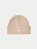 A ribbed knit beanie hat in a light beige or cream color, featuring a small tonal embroidered geometric logo on the front of the folded cuff, set against a solid off-white background.