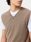 close up of Person wearing a brown sweater vest over a white shirt on a light background #color_taupe