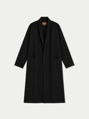 A black long coat with a shawl collar and front pockets, displayed flat against a light gray background. A small brown brand label is visible inside the collar.