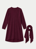 A long-sleeve high-low knit dress in deep burgundy, shown with a matching burgundy scarf tied to the right side, on a light gray background.