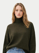 Woman wearing a dark green turtleneck sweater against a white background #color_capulet-olive