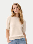 Woman wearing a beige sweater and blue jeans on a light gray background #color_off-white