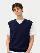 Man wearing a navy blue v neck vest over a white shirt on a light gray background #color_navy-blazer