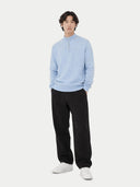 Person wearing a light blue cashmere sweater, black pants, and white shoes on a white background