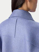 Close-up back view of a person wearing a light periwinkle blue wool-blend coat, showing the collar, back seam, and fabric texture against a plain off-white background.