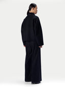 A model shown from the back wearing a black cropped long-sleeve jacket and matching wide-leg trousers against a plain light gray studio background.