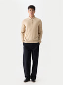 front view of a man wearing a beige sweater polo and black pants on a white background