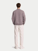 Person wearing a gray sweater and white pants on a light gray background #color_stucco