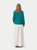 back view of a woman wearing a teal sweater and white skirt on a white background #color_dynasty-green