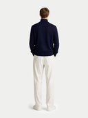 back view of a person wearing a navy sweater and white pants on a light gray background #color_navy-blazer