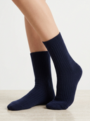 A pair of navy blue ribbed crew socks worn on a person's feet, shown against a clean white background with a light wood floor.