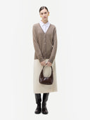 Person wearing a brown cardigan, white shirt, beige skirt, and black boots holding a brown handbag on a white background #color_taupe