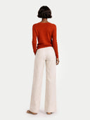 back view of a person wearing a rust-colored sweater and white pants on a light gray background #color_sugar-almond
