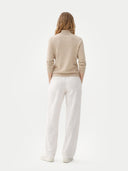 back view of a woman wearing a beige sweater and white pants on a light gray background #color_warm-grey