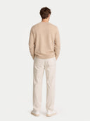 back view of a man wearing a beige sweater and white pants on a light gray background #color_warm-grey