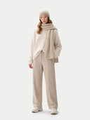 Person wearing a beige outfit with a sweater, scarf, and pants on a white background #color_warm-grey