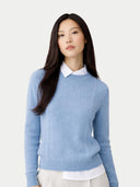 Woman wearing a light blue sweater over a white shirt on a plain background #color_dusty-blue
