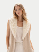 Woman wearing a beige vest with white fur trim on a light background #color_warm-grey