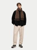 Man wearing a black jacket, beige pants, and a brown scarf on a white background