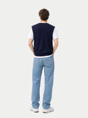 back view of a person wearing a navy vest, white shirt, and light blue jeans on a white background #color_navy-blazer