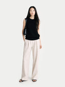 Front-view of a woman wearing a black sleeveless top and light-colored pants on a white background #color_black