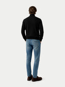 back view of a person wearing a black turtleneck and light blue jeans on a white background  #color_black