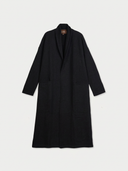 A long black shawl collar coat with a relaxed fit, displayed flat against a light gray background. A small brown brand label is visible inside the collar.