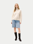 front view of a woman wearing a beige sweater, light blue denim shorts, and black knee-high boots on a white background #color_off-white